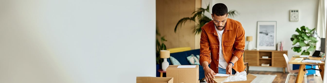 Mann stående ved spisebord pakker ting i esker