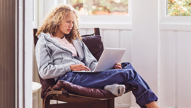 Ung kvinne sitter i en lenestol med laptop i fanget.