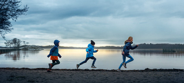 Tre barn løper langs en strand