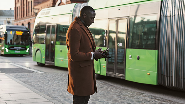 Mann ser på mobilen i en bussholdeplass