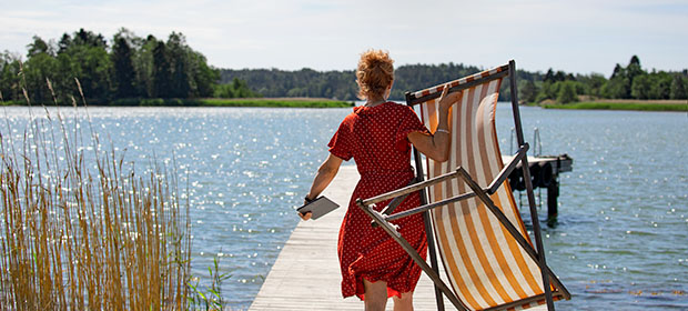 Kvinne sett bakfra gående ut på en brygge, mens hun bærer en solstol og et nettbrett.