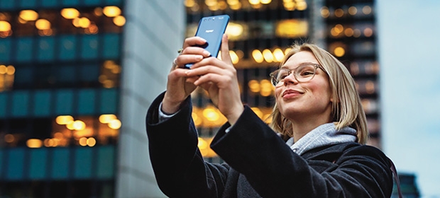 Kvinne smiler og tar selfie med mobilen