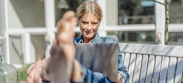 Kvinne sitter på en benk utenfor hytta med laptop i fanget og beina på bordet