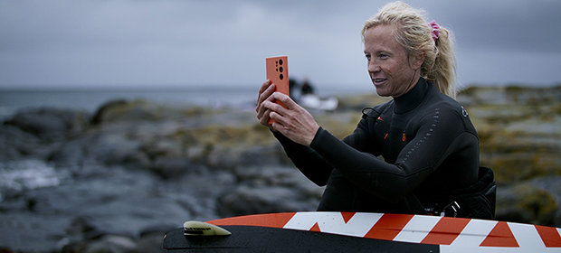 Kvinne med surfebrett og våtdrakt ser på mobilen