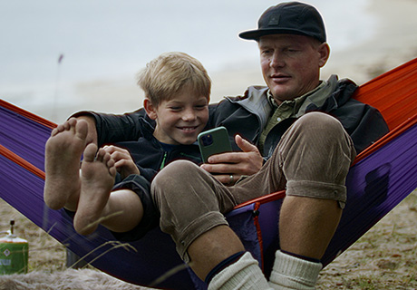 Far og sønn koser seg med mobilen i hengekøya