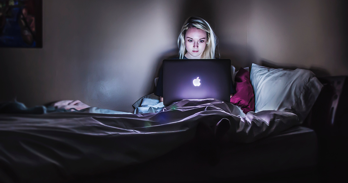 Jente sitter i sengen med mac og ser bekymret ut på grunn av netthets eller mobbing.