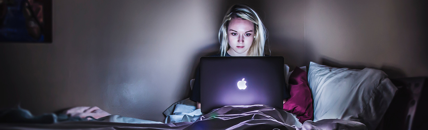 Jente sitter i sengen med mac og ser bekymret ut på grunn av netthets eller mobbing.