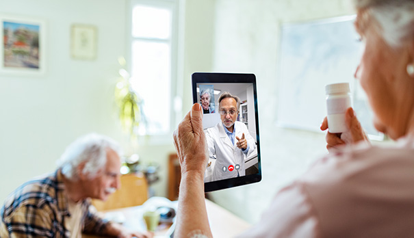 Eldre kvinne holder et nettbrett. På skjermen ser vi en lege som hun har en videosamtale med.