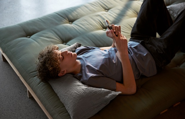 Ung mann ligger på sofaen med mobilen