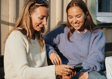 2 damer sitter ute og ser på en mobil