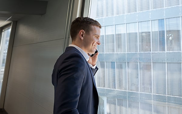 Mann i dress med telefon smiler og ser ut av vindu