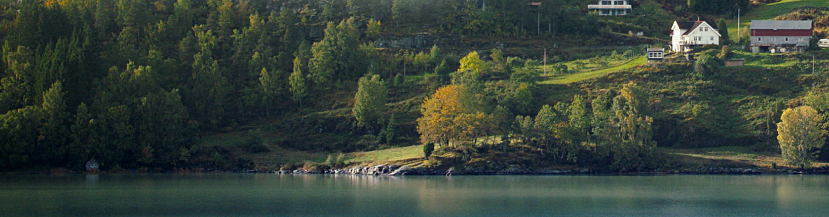 Utsikt mot gårdsbruk og skog med innsjø i front