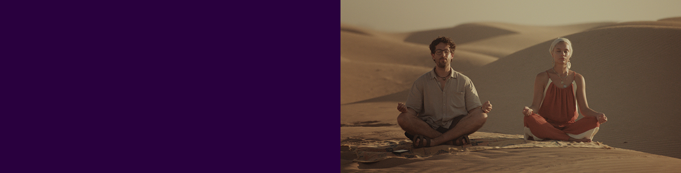 Ungt par i sanddyner i zen-modus. En mobil ligger i sanda ved han ene.
