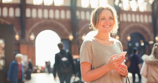 Ung kvinne på ferie med mobiltelefonen. Solfylt bybilde i bakgrunnen.