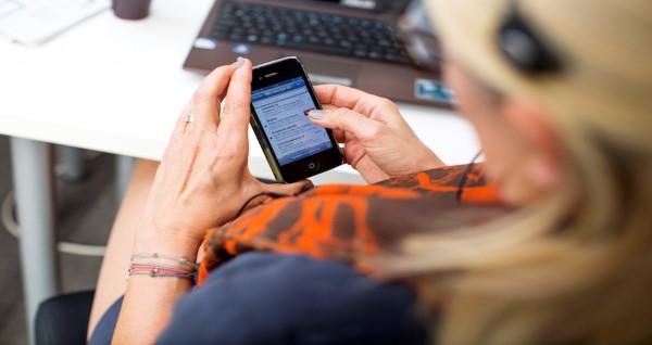 Dame i kontorlandskap sitter og ser på mobiltelefonen sin. Foto: Telia.