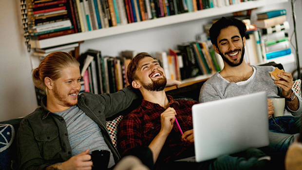 Tre menn i en sofa med laptop i fanget sitter og ler.