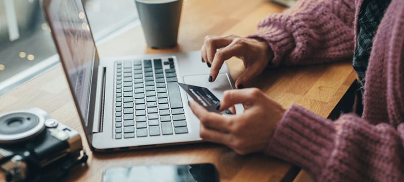 en dame jobber på pc og holder en bankkort
