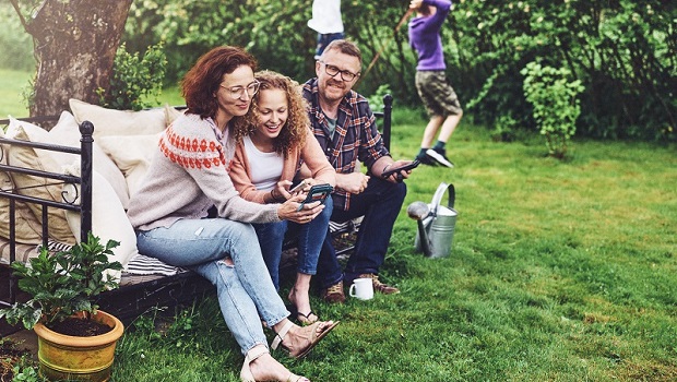 Blid familie på en benk i hagen med mobilen