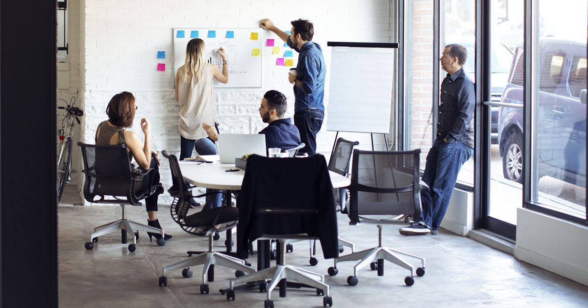 5 personer i et arbeidsrom med post-it-lapper og tavle gjennomfører en designsprint. 