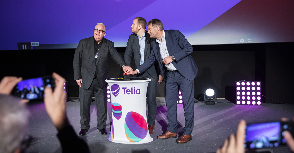 Tre menn trykker på en knapp foran en stor kinoskjerm.