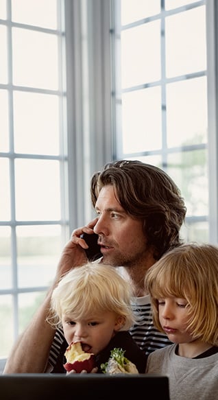 Far snakker i mobilen med to små barn i fanget. Barna ser på et nettbrett.