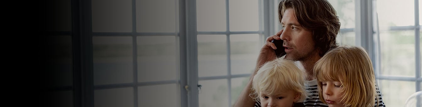 Far snakker i mobilen med to små barn i fanget. Barna ser på et nettbrett.