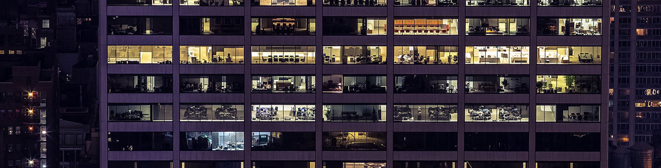 Kontorbygg sett utenfra en mørk kveld. Lys står på i store deler av bygget, man kan se inn i kontorlandskapet.