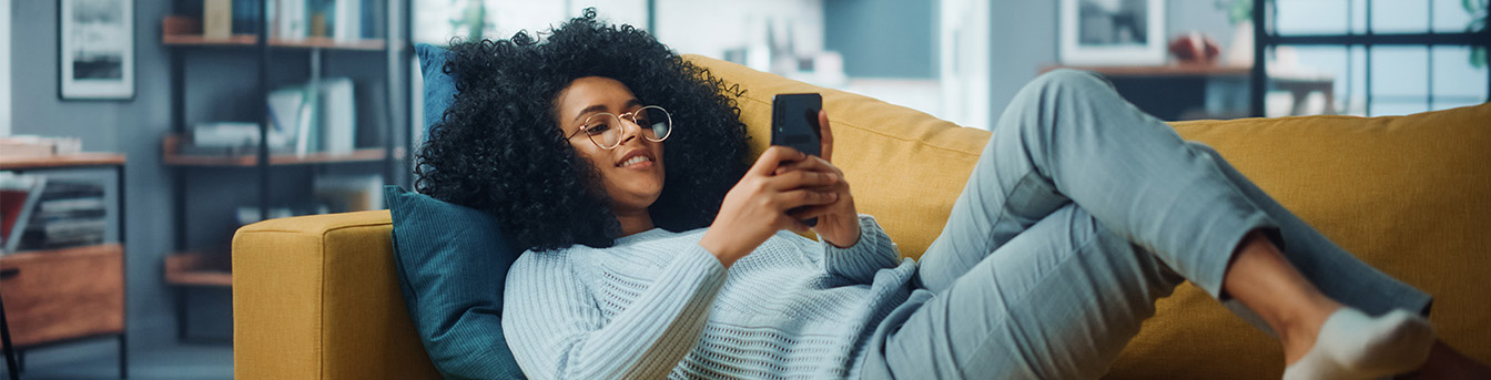 En dame ligger på en sofa mens hun surfer på telefonen
