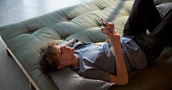 Ung gutt slapper av på en divan og ser på mobilen sin