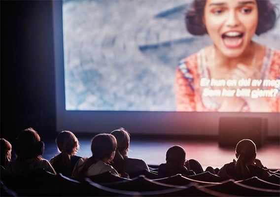 Kinosal hvor en film vises på lerretet. Vi ser noen rader bakfra med publikum som ser film i kinomørket.