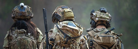 Tre militæruniformerte personer med kamuflasje-uniformer og hjelm sett bakfra.