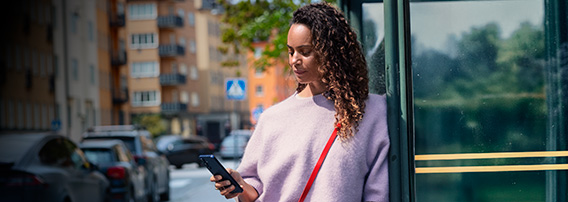 Ung kvinne med mobil står i gaten i byen en tidlig høstdag eller sein sommerdag