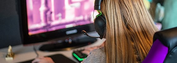 Jente sett bakfra mens hun sitter i gamingstol foran PC og spiller.