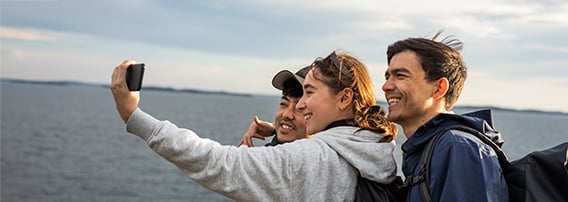 Ungdommer i hettejakker tar selfie ved sjøen