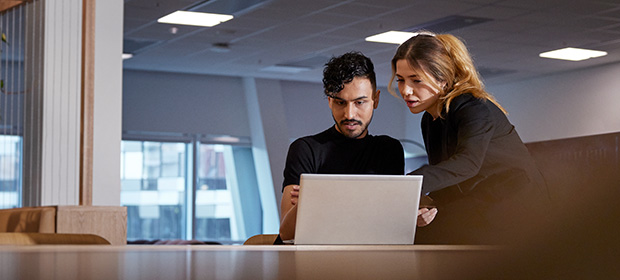 Mann og kvinne i kontorlandskap ser på en laptop.