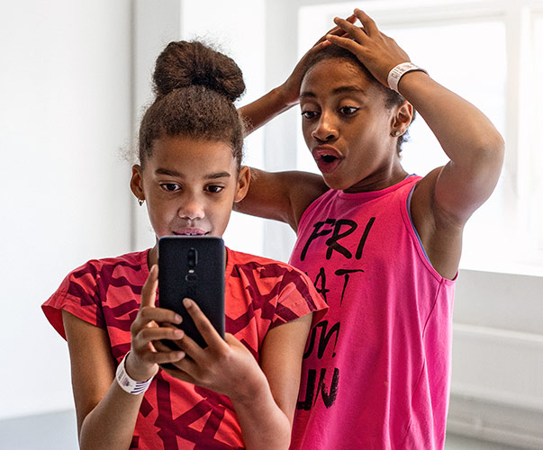 En ung jente holder opp mobilen. En annen jente ser på skjermen sammen med henne, med et overrasket uttrykk.