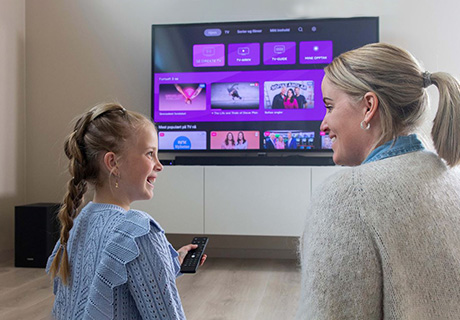 En jente og en kvinne sitter på gulvet foran en TV som vider menyen til Telia Play