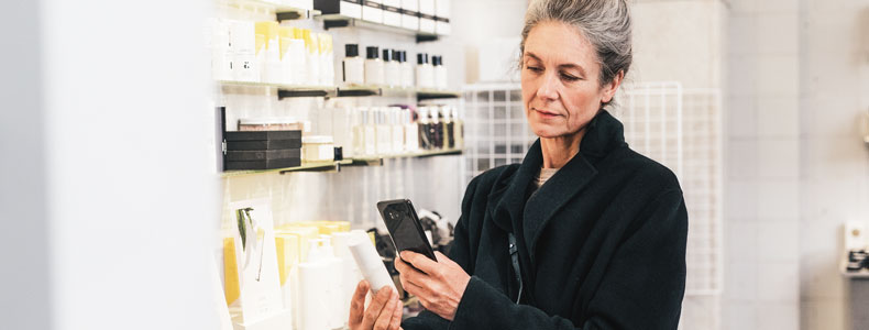 Voksen dame står i butikk og holder holder opp en ny telefon.