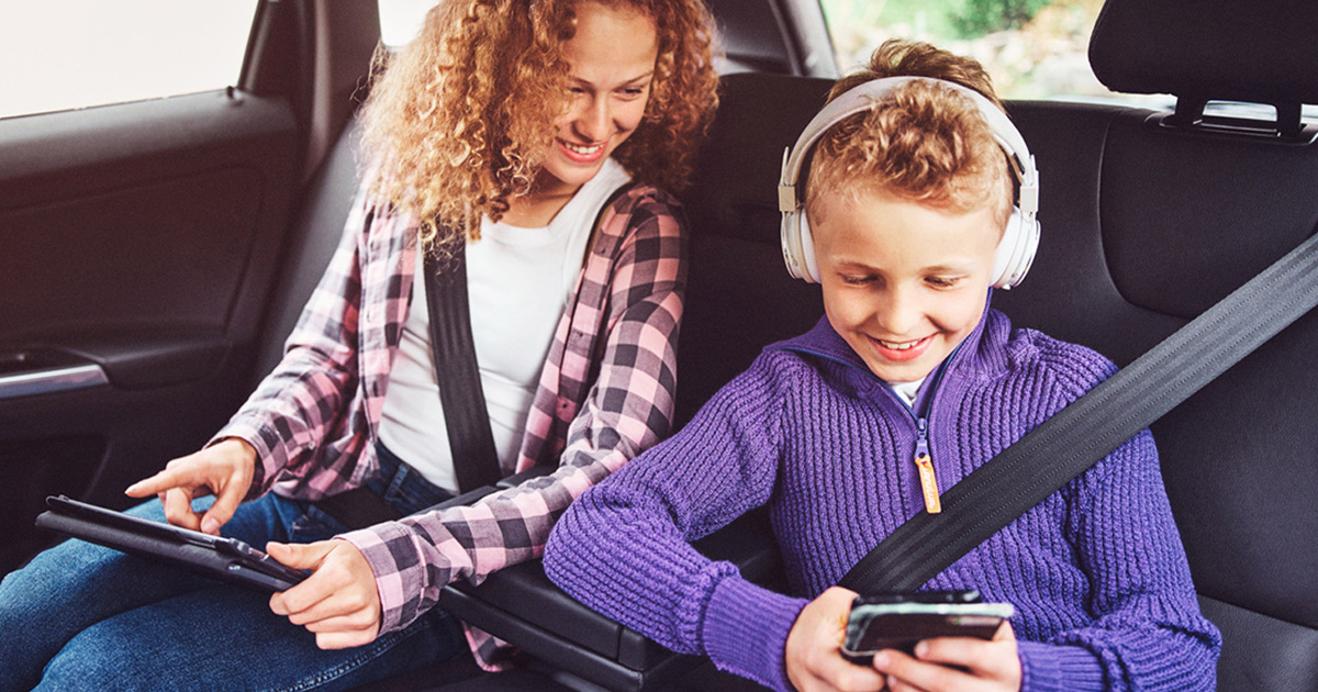 To barn i bil med nettbrett og mobil