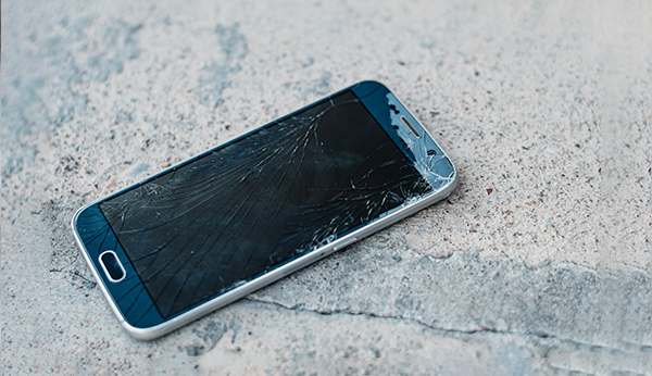 Mobiltelefon med skadet skjerm liggende på bakken, sett ovenfra. Mobiltelefon med skadet skjerm liggende på bakken, sett ovenfra.