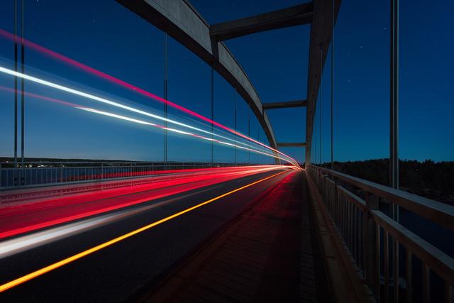 Bro i mørket hvor det er fotografert slik at bilene danner en lysstripe.