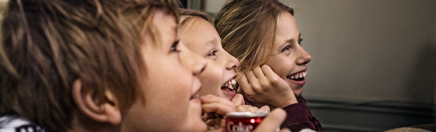 Smilende barn i profil, de ser trolig på TV