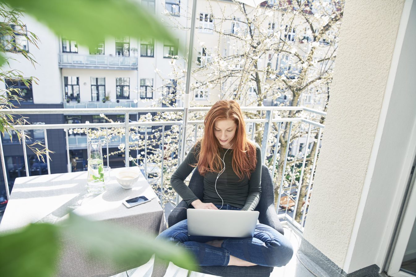 A redhaired girl sits on a balcony with her laptop in her lap. A redhaired girl sits on a balcony with her laptop in her lap.