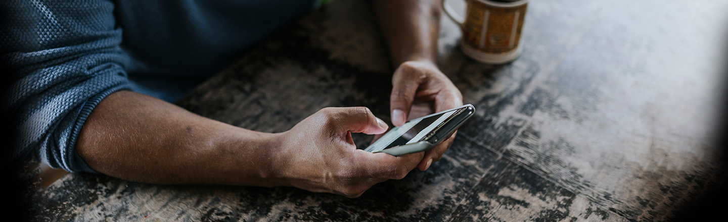 En arm holder i en telefon foran en kaffekopp på et bord