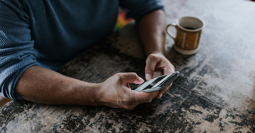 En arm holder i en telefon foran en kaffekopp på et bord