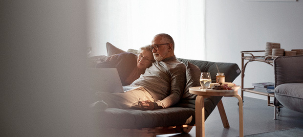 Et par ligger på en sofa mens de ser på en laptop