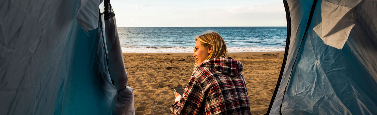 Ung dame sitter i teltet sitt på sandstrand.