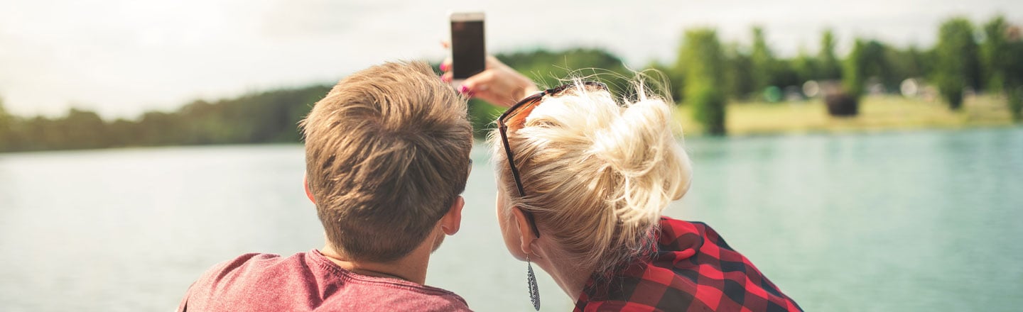 To ungdommer sitter på en brygge og tar selfie sammen.