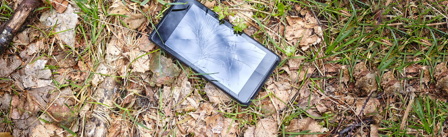 Mobiltelefon med knust skjerm som ligger på en plen.
